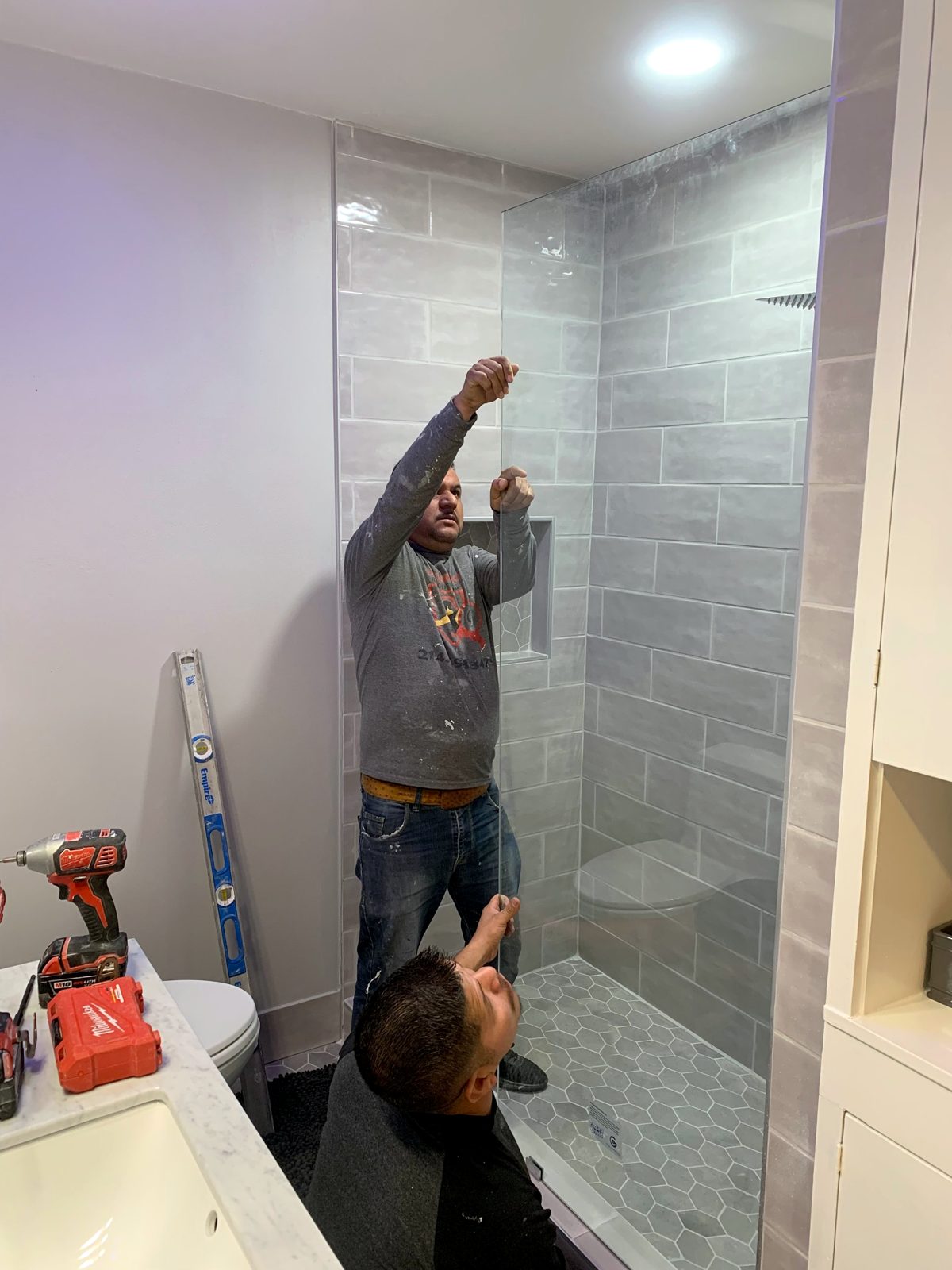 Two Guerrero Remodeling crew members setting a frameless glass shower panel