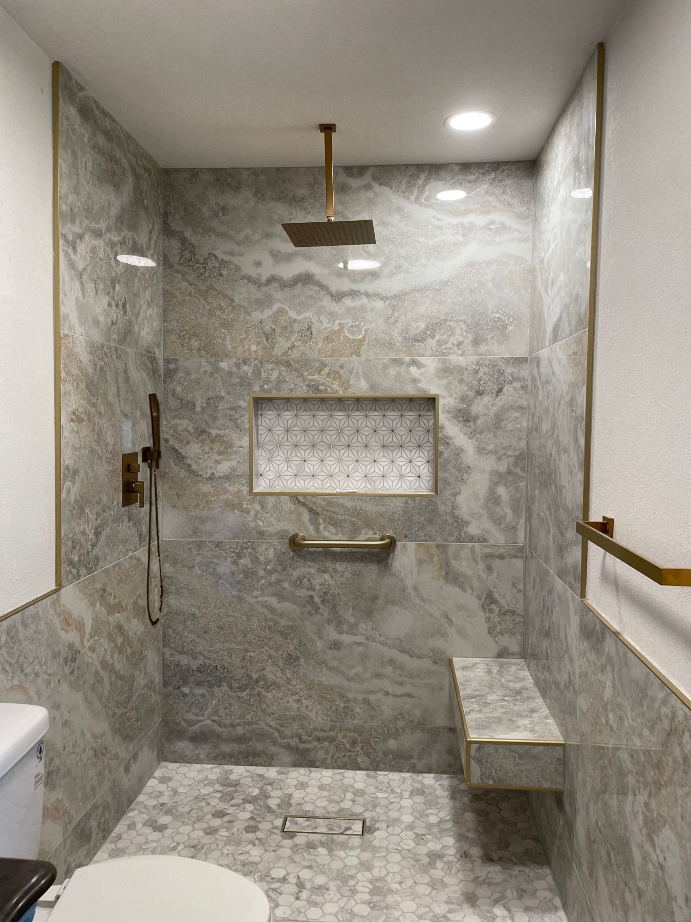 Walk-in shower in large-format porcelain tile with brushed gold rain head, hand shower, trim and a patterned tile niche
