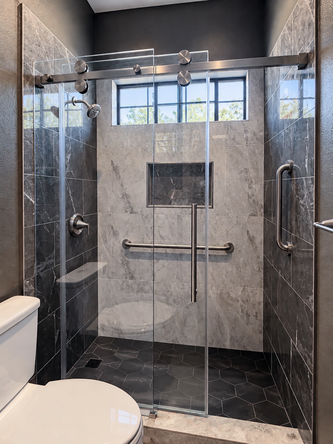 Gray marble-look shower with a sliding glass door, bench and lit niche